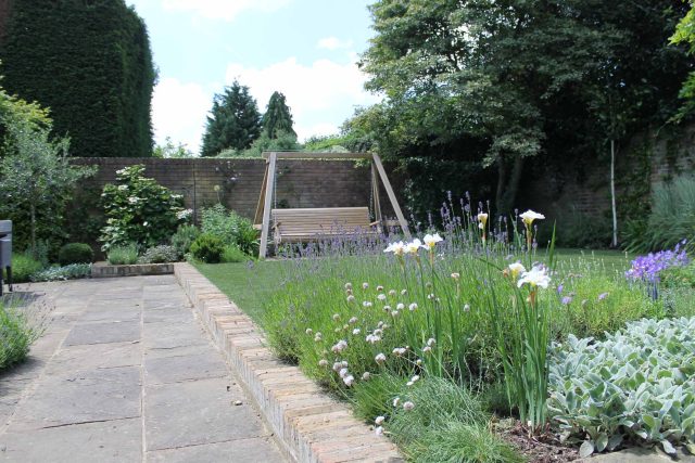 York stone paving leads across a lawn to a garden swing in luxury Wimbledon.