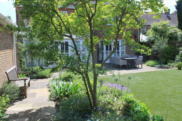 A Yorkstone path and a garden bench sit on a luxury artificial lawn in Wimbledon.
