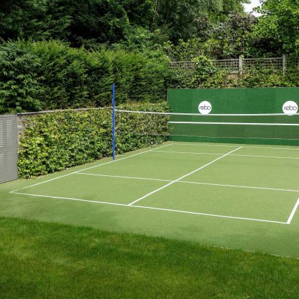 Large family garden design with outdoor kitchen, terrace, lighting, evergreens, lawn and stone-clad retaining wall designers specialist contractors in London.