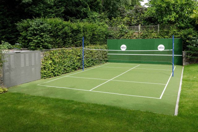 Large family garden design with outdoor kitchen, terrace, lighting, evergreens, lawn and stone-clad retaining wall designers specialist contractors in London.