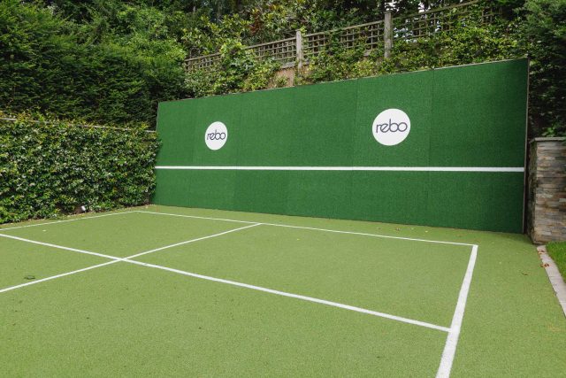 Large family garden design with outdoor kitchen, terrace, lighting, evergreens, lawn and stone-clad retaining wall designers specialist contractors in London.