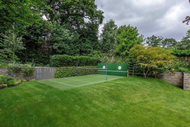 Large family garden design with outdoor kitchen, terrace, lighting, evergreens, lawn and stone-clad retaining wall designers specialist contractors in London.