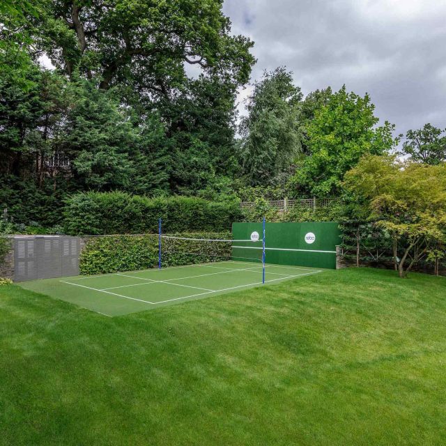 Large family garden design with outdoor kitchen, terrace, lighting, evergreens, lawn and stone-clad retaining wall designers specialist contractors in London.