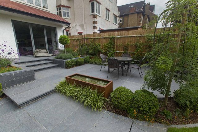 Family Garden, upper and lower stone terrance, wrapped with lawn, hidden trampoline Basalt terraces woodland planting Muswell Hill London design specialists.