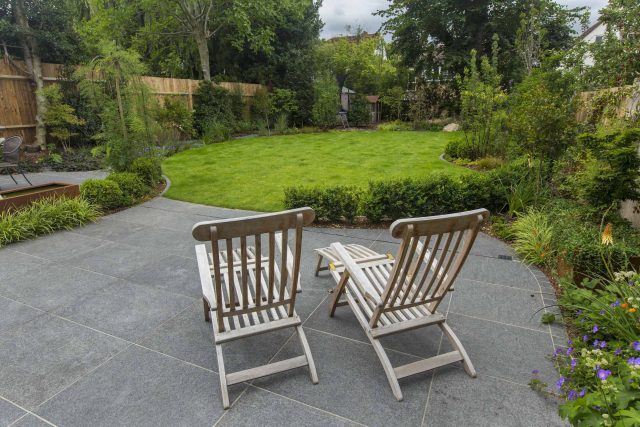 Family Garden, upper and lower stone terrance, wrapped with lawn, hidden trampoline Basalt terraces woodland planting Muswell Hill London design specialists.