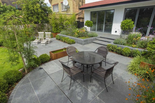 Family Garden, upper and lower stone terrance, wrapped with lawn, hidden trampoline Basalt terraces woodland planting Muswell Hill London design specialists.