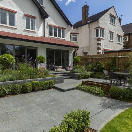 Family Garden, upper and lower stone terrance, wrapped with lawn, hidden trampoline Basalt terraces woodland planting Muswell Hill London design specialists.