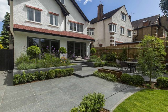 Family Garden, upper and lower stone terrance, wrapped with lawn, hidden trampoline Basalt terraces woodland planting Muswell Hill London design specialists.