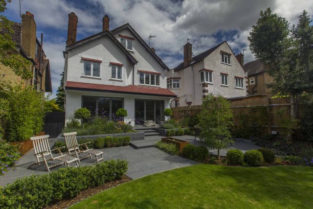Family Garden, upper and lower stone terrance, wrapped with lawn, hidden trampoline Basalt terraces woodland planting Muswell Hill London design specialists.