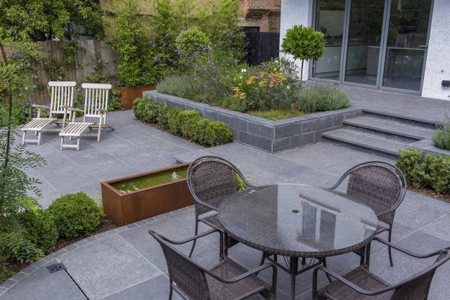 Family Garden, upper and lower stone terrance, wrapped with lawn, hidden trampoline Basalt terraces woodland planting Muswell Hill London design specialists.