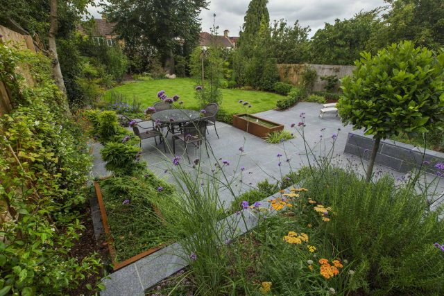 Family Garden, upper and lower stone terrance, wrapped with lawn, hidden trampoline Basalt terraces woodland planting Muswell Hill London design specialists.