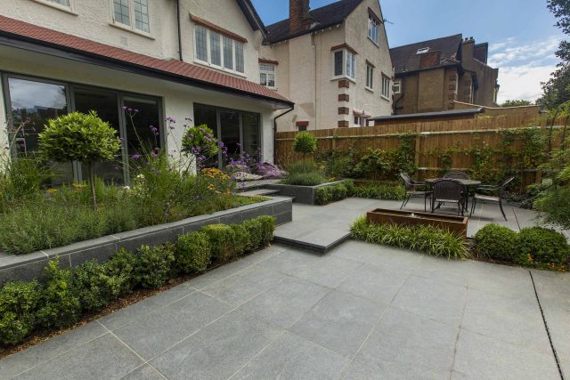 Family Garden, upper and lower stone terrance, wrapped with lawn, hidden trampoline Basalt terraces woodland planting Muswell Hill London design specialists.
