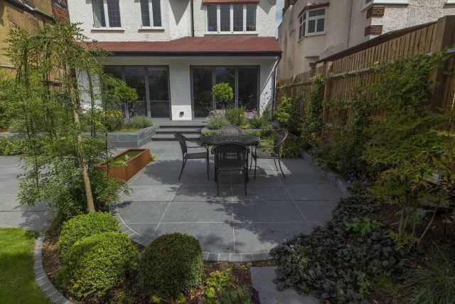Family Garden, upper and lower stone terrance, wrapped with lawn, hidden trampoline Basalt terraces woodland planting Muswell Hill London design specialists.