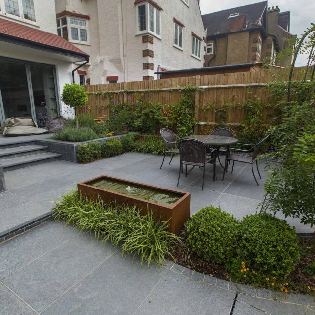 Family Garden, upper and lower stone terrance, wrapped with lawn, hidden trampoline Basalt terraces woodland planting Muswell Hill London design specialists.