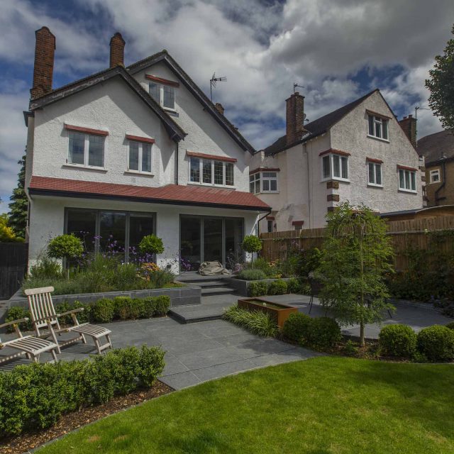 Family Garden, upper and lower stone terrance, wrapped with lawn, hidden trampoline Basalt terraces woodland planting Muswell Hill London design specialists.