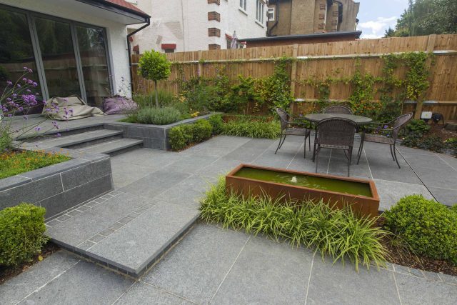 Family Garden, upper and lower stone terrance, wrapped with lawn, hidden trampoline Basalt terraces woodland planting Muswell Hill London design specialists.