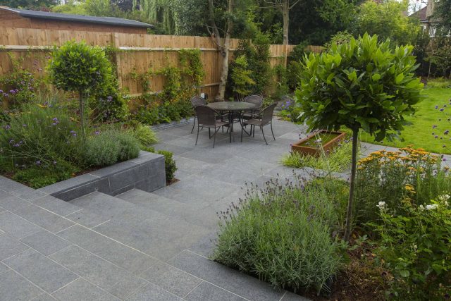 Family Garden, upper and lower stone terrance, wrapped with lawn, hidden trampoline Basalt terraces woodland planting Muswell Hill London design specialists.