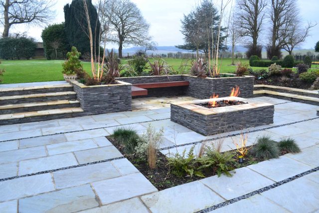 Contemporary courtyard garden in a rural setting paving riven grey sand stone and black polished pebbles, floating hardwood built-in bench seat Hertfordshire.