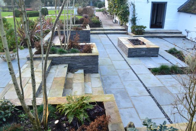 Contemporary courtyard garden in a rural setting paving riven grey sand stone and black polished pebbles, floating hardwood built-in bench seat Hertfordshire.