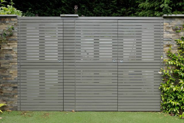 Large family garden design with outdoor kitchen, terrace, lighting, evergreens, lawn and stone-clad retaining wall designers specialist contractors in London.