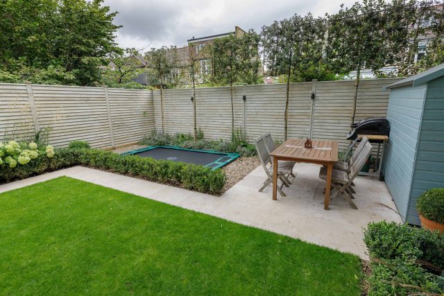 Family garden design in Barnes West London, lawn space as possible for various play activities and an intimate dining area with pleached Quercus Ilex trees.
