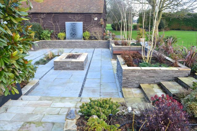 Contemporary courtyard garden in a rural setting paving riven grey sand stone and black polished pebbles, floating hardwood built-in bench seat Hertfordshire.