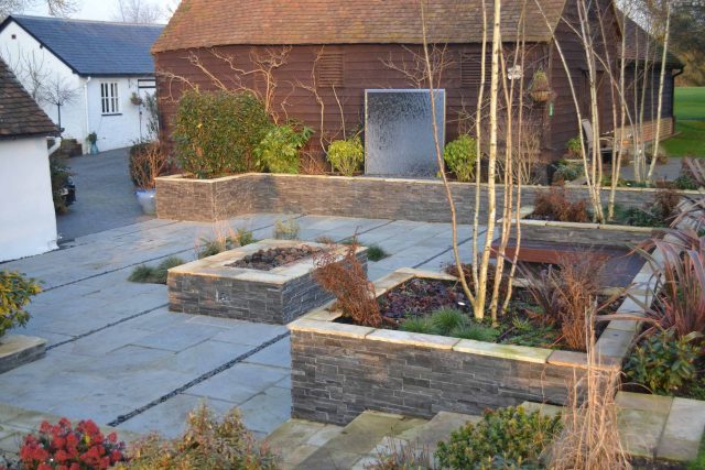 Contemporary courtyard garden in a rural setting paving riven grey sand stone and black polished pebbles, floating hardwood built-in bench seat Hertfordshire.
