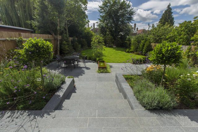 Family Garden, upper and lower stone terrance, wrapped with lawn, hidden trampoline Basalt terraces woodland planting Muswell Hill London design specialists.