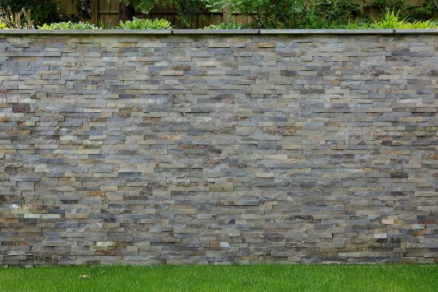 Large family garden design with outdoor kitchen, terrace, lighting, evergreens, lawn and stone-clad retaining wall designers specialist contractors in London.