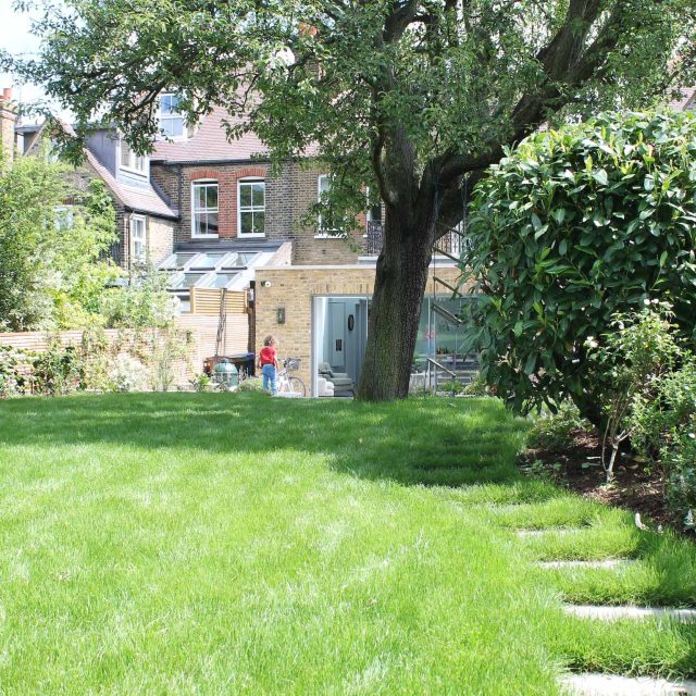Summer Orchard Garden in Dulwich landscaper with canopies of the fruit trees and flowers designed Sarah Hammond trampoline area, stepping stones natural lawn.