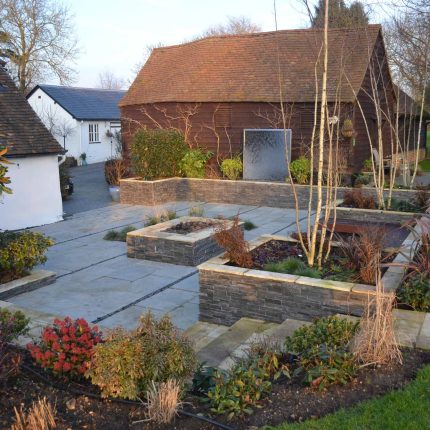 Contemporary courtyard garden in a rural setting paving riven grey sand stone and black polished pebbles, floating hardwood built-in bench seat Hertfordshire.