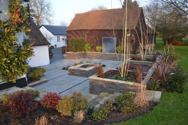 Contemporary courtyard garden in a rural setting paving riven grey sand stone and black polished pebbles, floating hardwood built-in bench seat Hertfordshire.