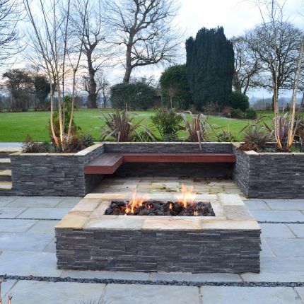 Contemporary courtyard garden in a rural setting paving riven grey sand stone and black polished pebbles, floating hardwood built-in bench seat Hertfordshire.