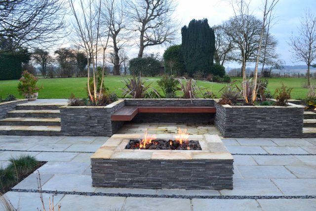 Contemporary courtyard garden in a rural setting paving riven grey sand stone and black polished pebbles, floating hardwood built-in bench seat Hertfordshire.