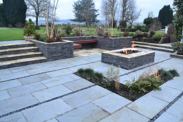 Contemporary courtyard garden in a rural setting paving riven grey sand stone and black polished pebbles, floating hardwood built-in bench seat Hertfordshire.