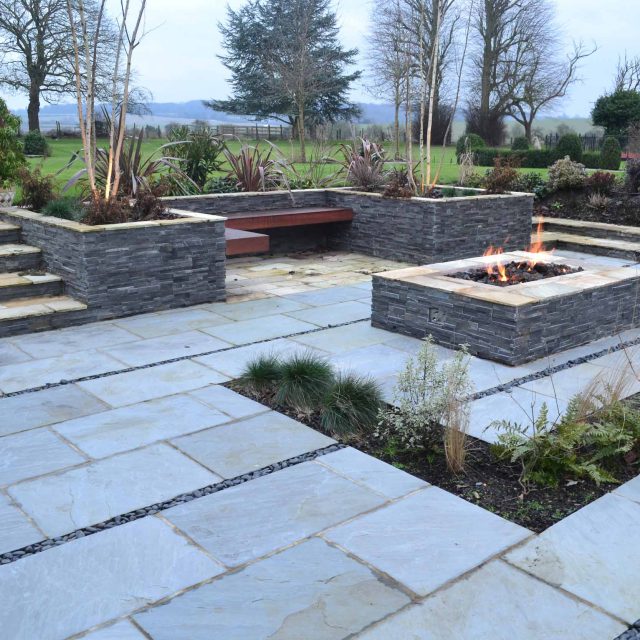 Contemporary courtyard garden in a rural setting paving riven grey sand stone and black polished pebbles, floating hardwood built-in bench seat Hertfordshire.