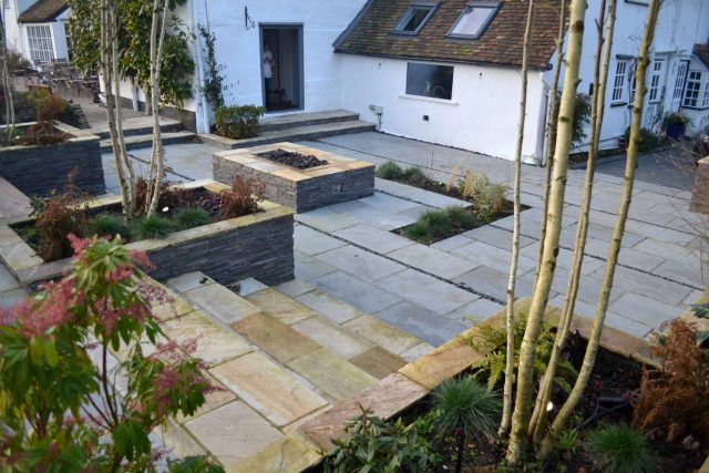 Contemporary courtyard garden in a rural setting paving riven grey sand stone and black polished pebbles, floating hardwood built-in bench seat Hertfordshire.