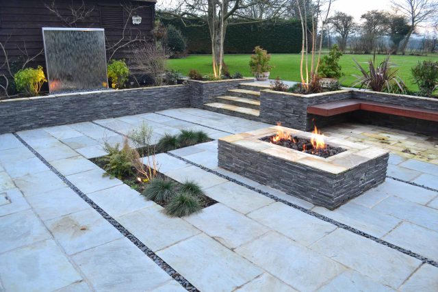 Contemporary courtyard garden in a rural setting paving riven grey sand stone and black polished pebbles, floating hardwood built-in bench seat Hertfordshire.
