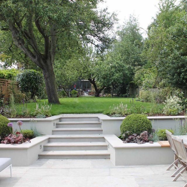 Summer Orchard Garden in Dulwich landscaper with canopies of the fruit trees and flowers designed Sarah Hammond trampoline area, stepping stones natural lawn.