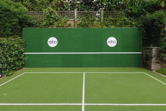 Large family garden design with outdoor kitchen, terrace, lighting, evergreens, lawn and stone-clad retaining wall designers specialist contractors in London.