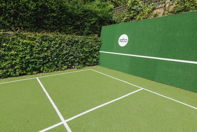 Large family garden design with outdoor kitchen, terrace, lighting, evergreens, lawn and stone-clad retaining wall designers specialist contractors in London.