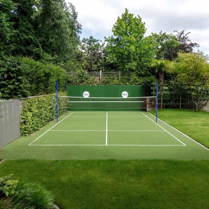 Large family garden design with outdoor kitchen, terrace, lighting, evergreens, lawn and stone-clad retaining wall designers specialist contractors in London.