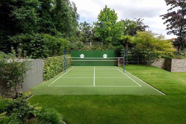 Large family garden design with outdoor kitchen, terrace, lighting, evergreens, lawn and stone-clad retaining wall designers specialist contractors in London.